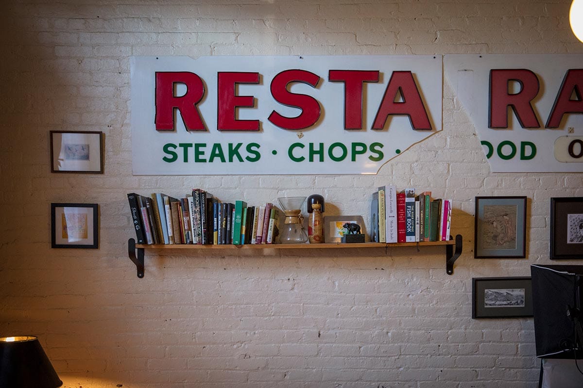 A white, brick wall with a bookshelf, signs, and personal framed photos of Tejal Rao.