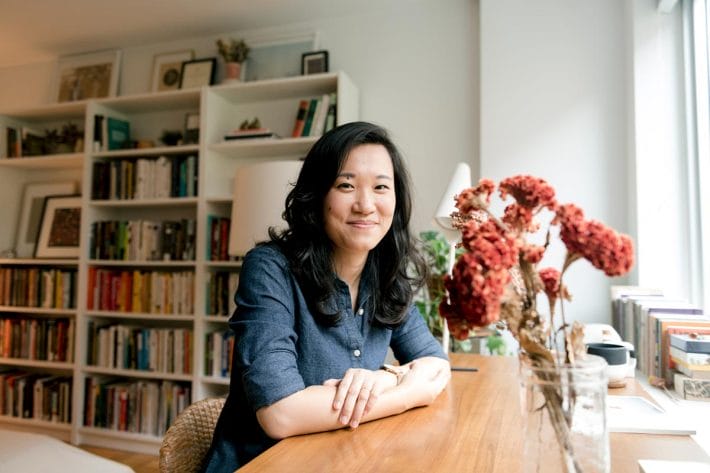 Jenny Xie sitting at a desk in front of a bookcase of literature in a light-filled room.