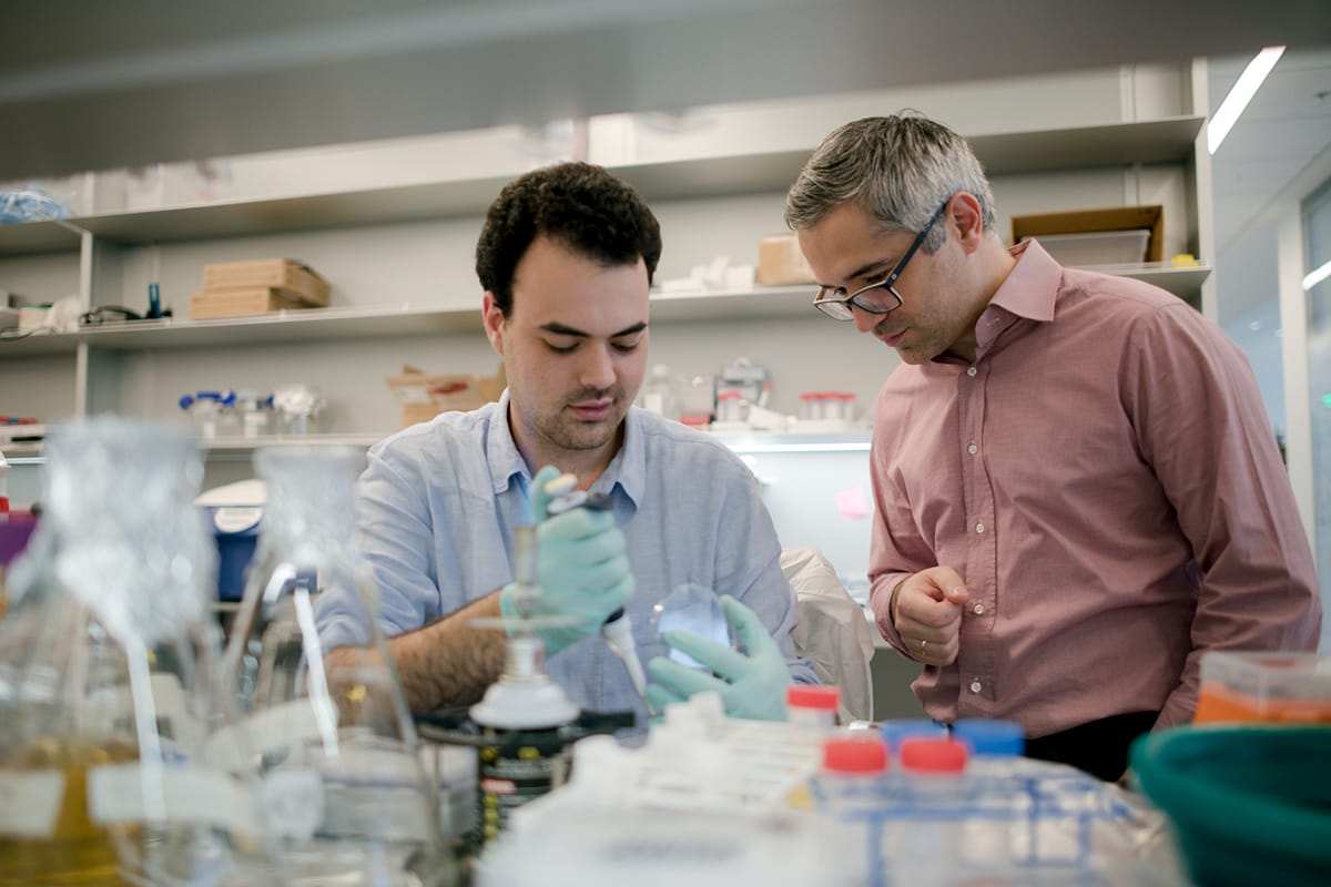 Biomedical researcher Kivanc Birsoy watches a Rockefeller University student conduct an experiment at a lab bench.