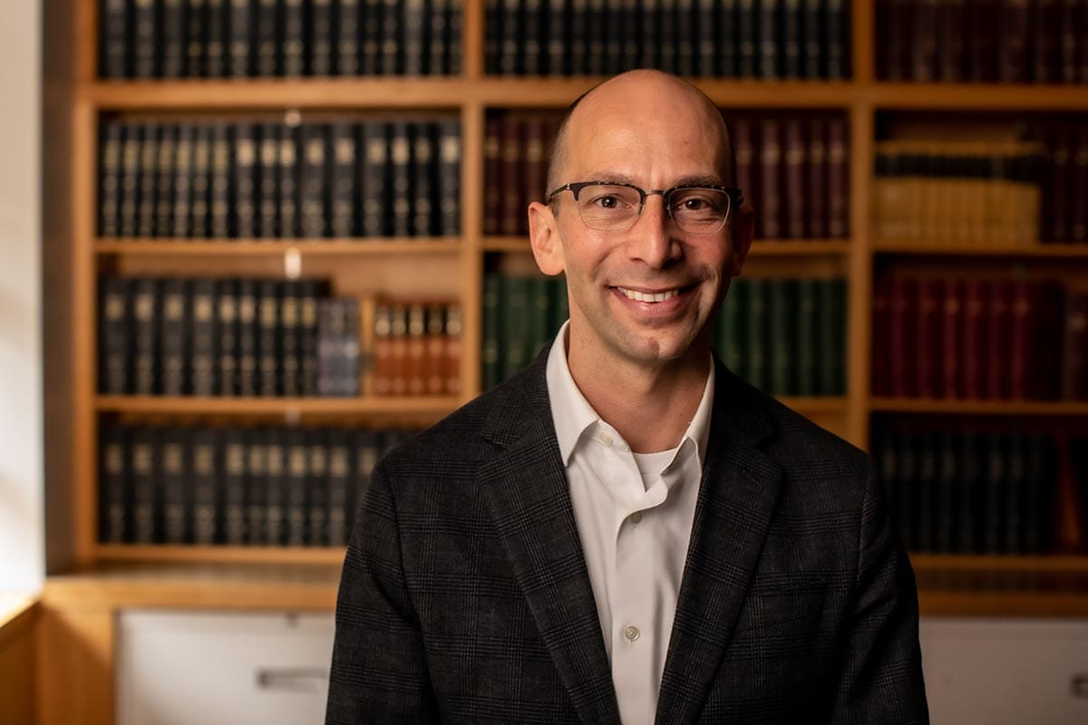 Portrait of Martin Jonikas, in suit jacket, in front of a library shelf of medical journals.