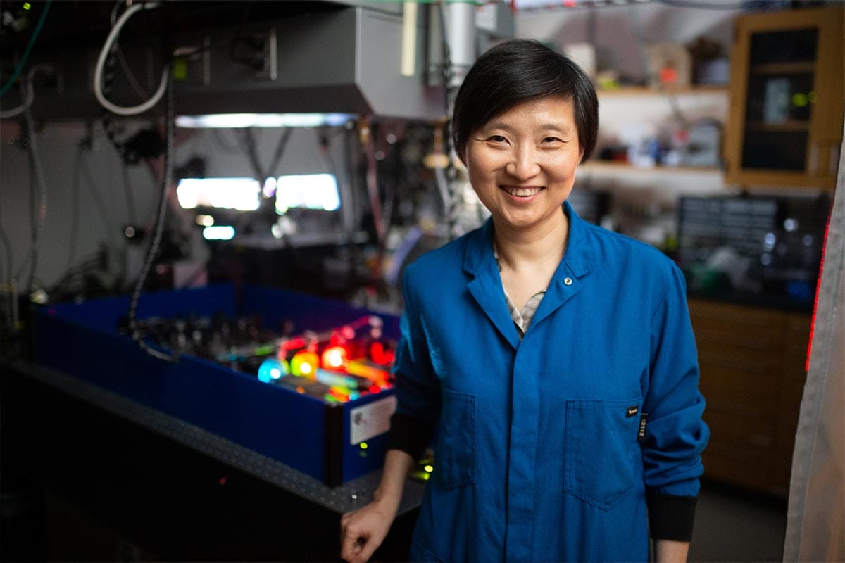 Xiaowei Zhuang, wearing a blue Harvard University lab coat, stands in front of a custom-built STORM microscope.