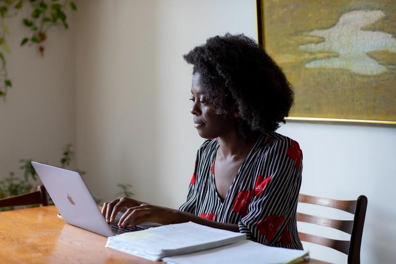 Yaa Gyasi typing on a laptop with novel manuscripts by her side.