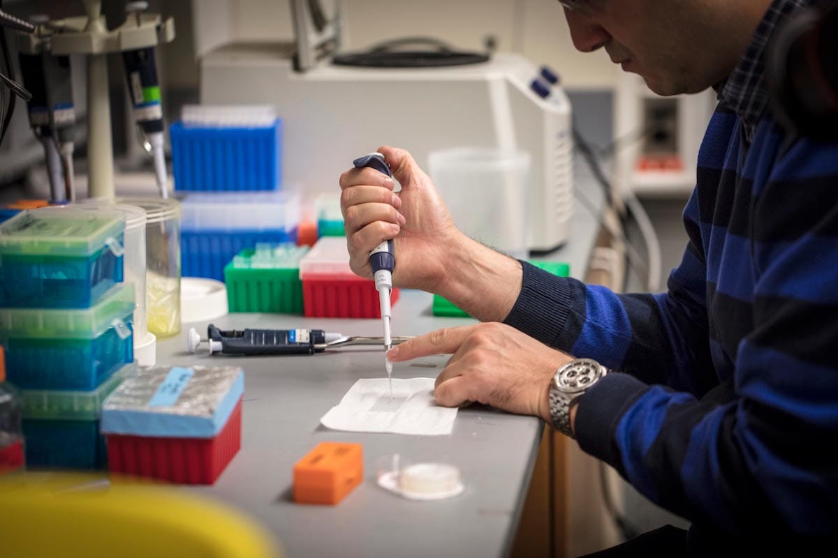 Ahmet Yildiz's arms and hands are the focus of the image as he sits testing a sample, surrounded by lab apparatus.