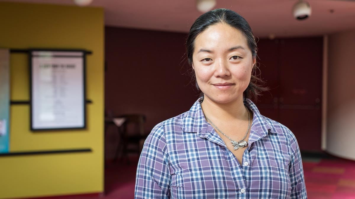 Desdemona Chiang is pictured from the chest-up standing outside the house doors of a theater, wearing a flannel button-down.