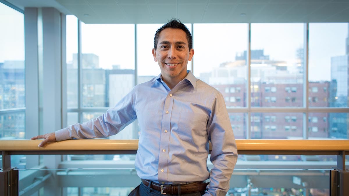 Fernando Camargo is pictured standing on a balcony with high-rise buildings visible through glass windows behind him.