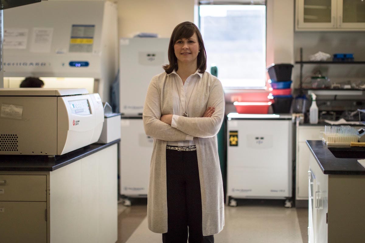Michaela Gack stands in the center of the image with her arms folded, surrounded by lab equipment.