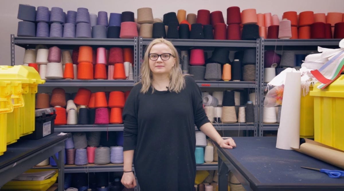 Natallia Pilipenka is pictured in front of shelves filled with multiple spools of thread in various colors.