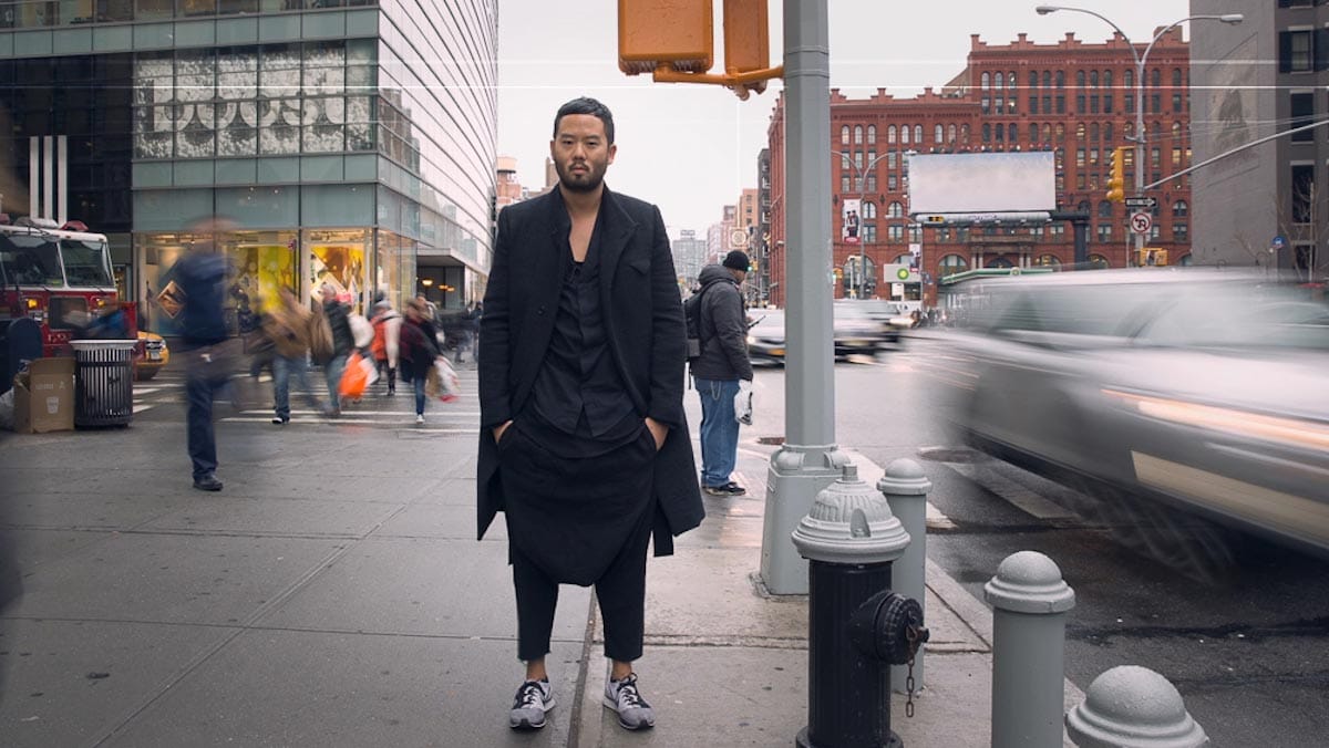 Siki Im, wearing a long black coat, stands on the bustling corner of two New York City streets.