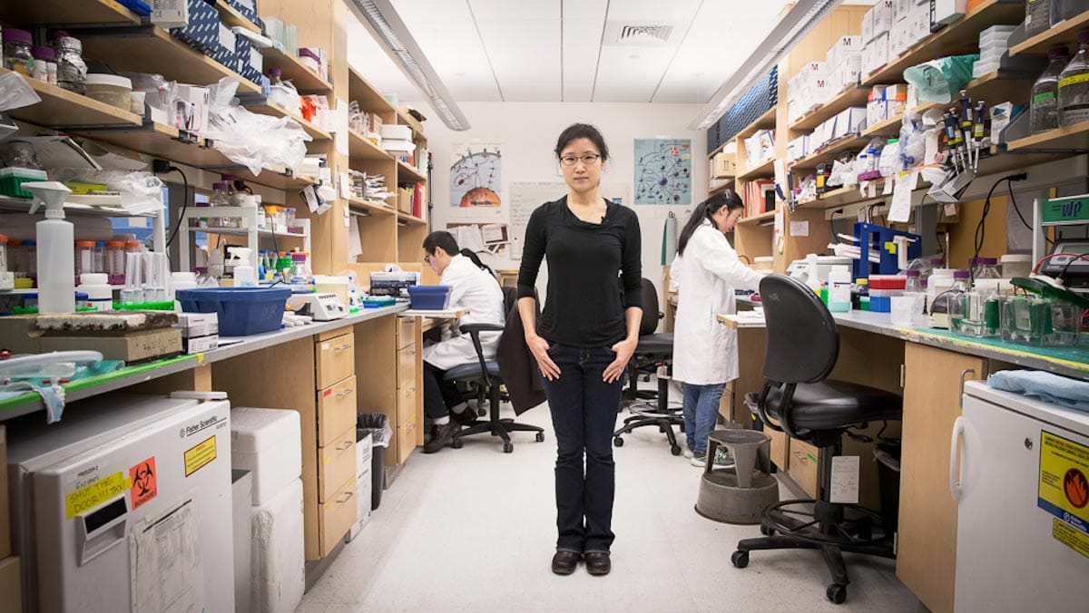 Sun Hur stands on the floor of a laboratory surrounded by lab apparatus and equipment.