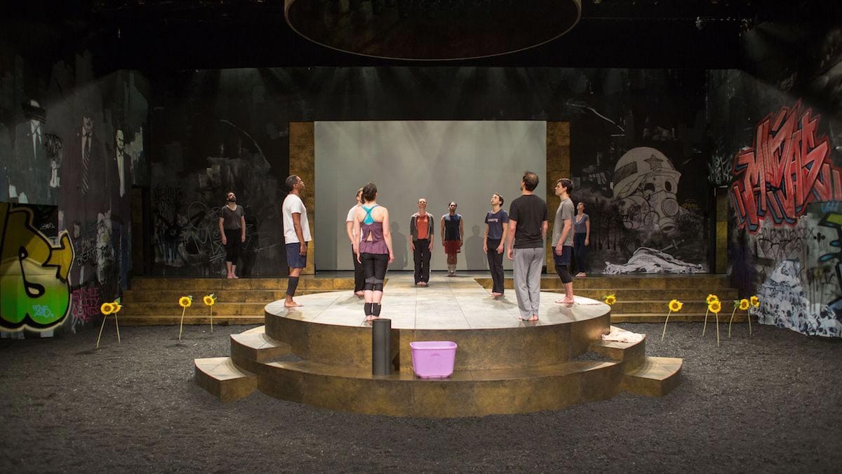 The cast of the Wilma Theater's "Rosencrantz and Guildenstern Are Dead" (2015) as they stand dispersed across a stage and a circular platform with graffiti painted backdrops behind them.