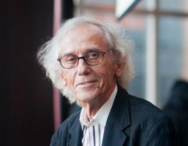 A photo of Christo in front of a wall of windows.