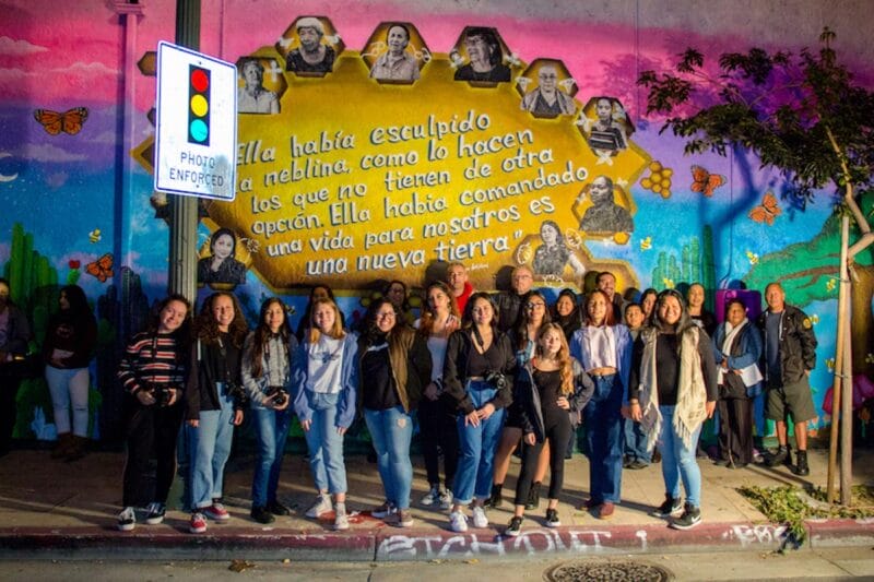 A group of teenage girls standing in front of a multi-colored mural.