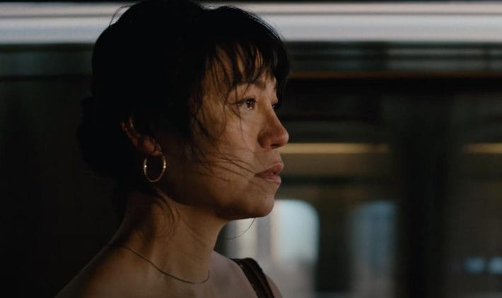 A close-up and side-profile of the protagonist in Lingua Franca, Olivia, with a subway train in the background.
