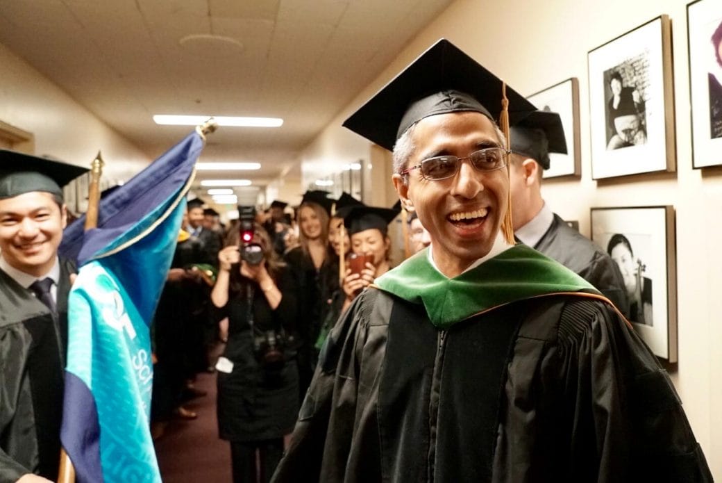 Vivek Murthy, smiling in a cap and gown, surrounded by graduating students and faculty at the University of Hawaii.