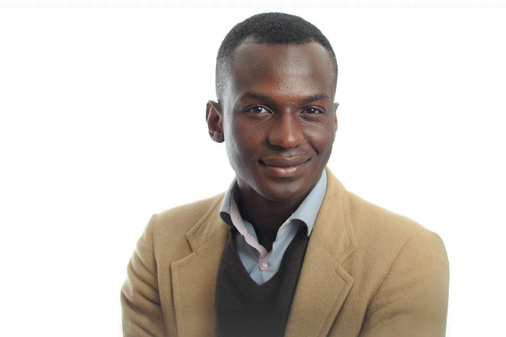 Ibrahim Cissé, wearing a tan suit, against a white backdrop.