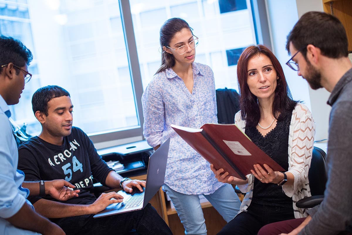 Silvi Rouskin holding a report and talking with graduate students.