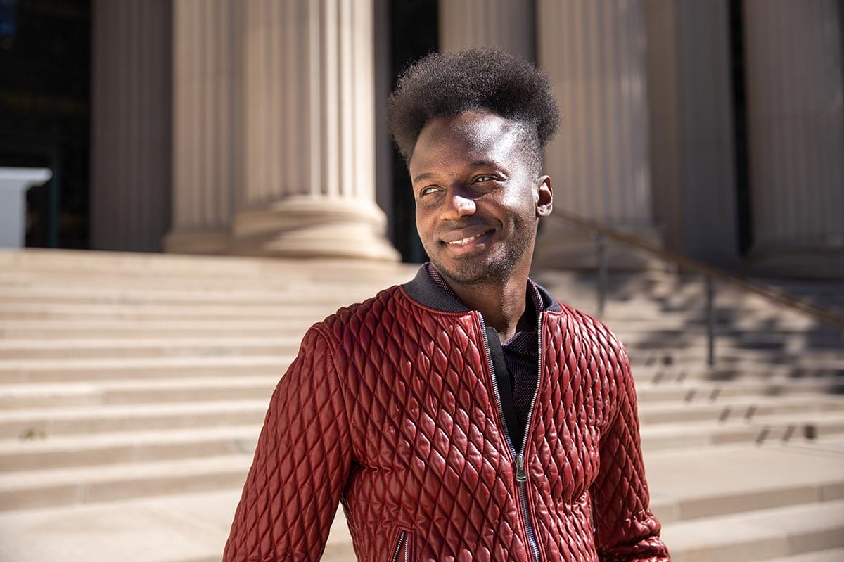 Ibrahim, in a red coat, stands in front of steps at MIT.