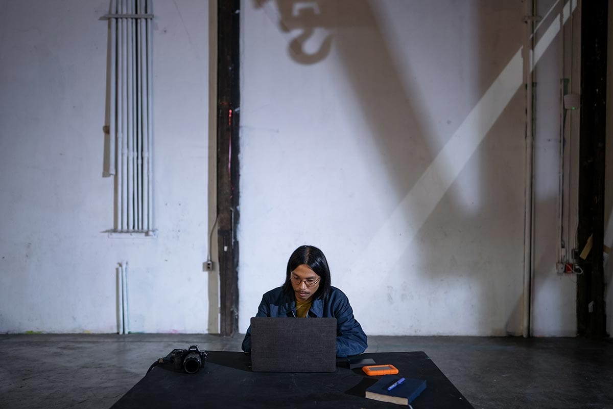 Miko sitting at a table in a large room working on a laptop.