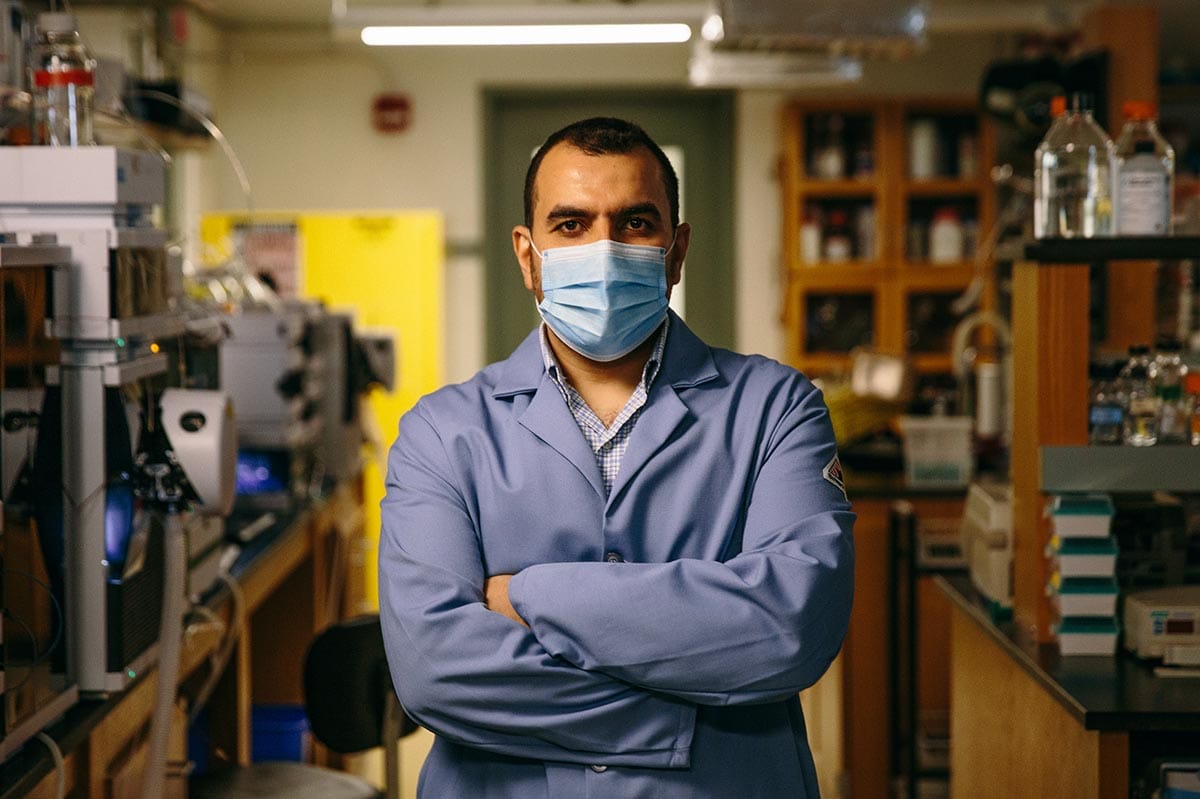Mohamed, arms crossed and wearing a lab coat, stands in his Princeton University lab.