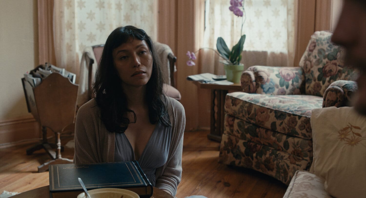 A film still of Olivia, a Filipina trans woman, looking off-screen while sitting by a coffee table.