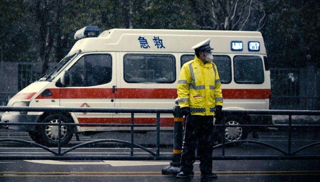 A still frame of an officer stands in front of an ambulance, from the film 76 Days.
