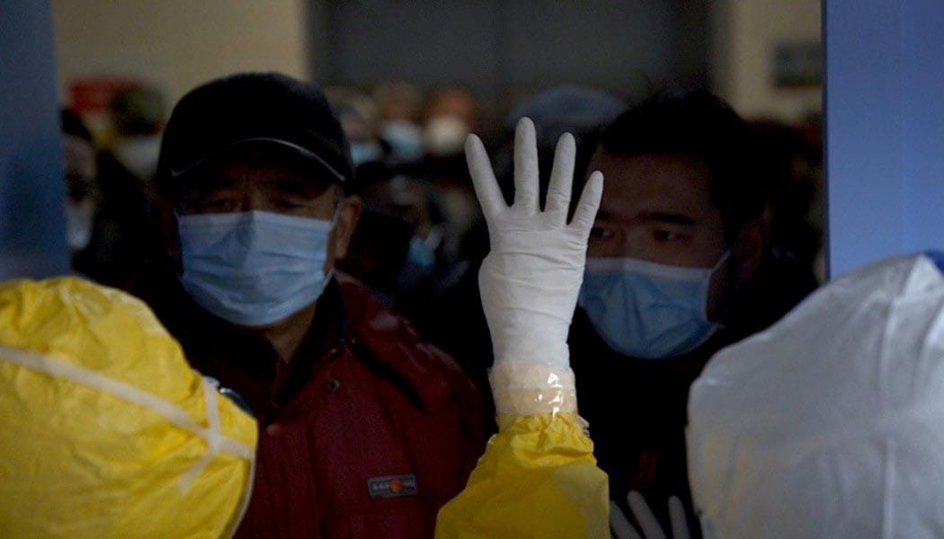 A crowd of people are separated by a door and medical personnel wearing PPE.