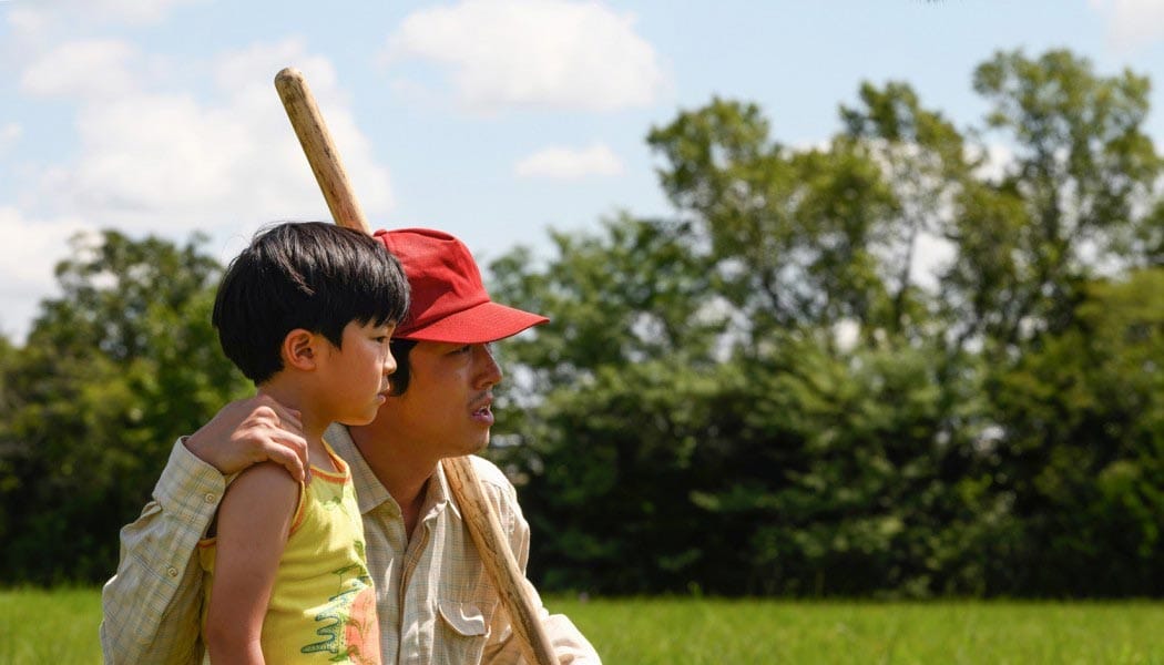 A film still of Steven Yeun, wearing a red hat, with arm around his on-screen son.