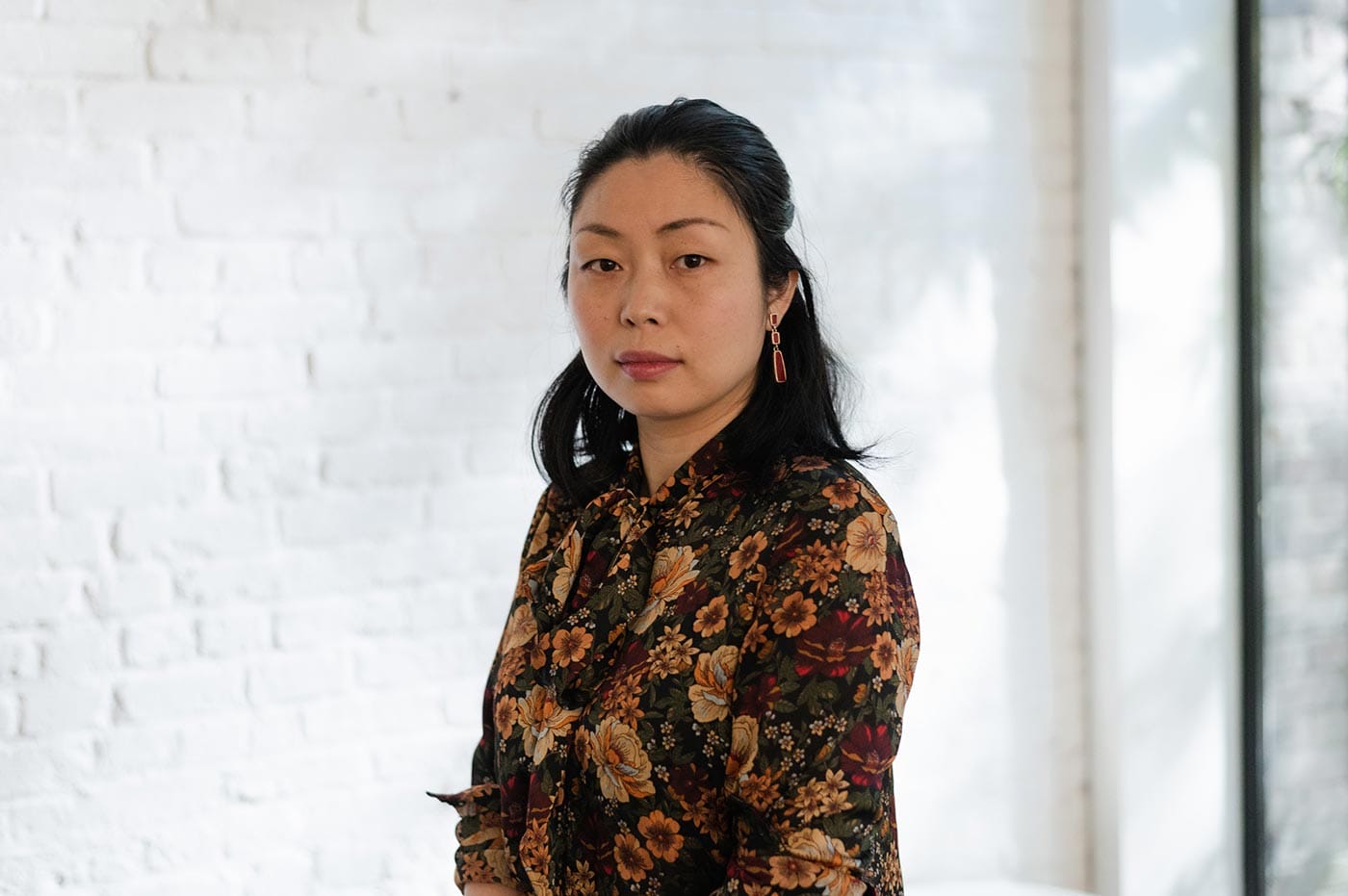 Nanfu Wang, in a floral shirt, standing in front of a white brick wall.