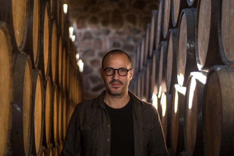 Juan Pablo González standing in a cellar surrounded by barrels.