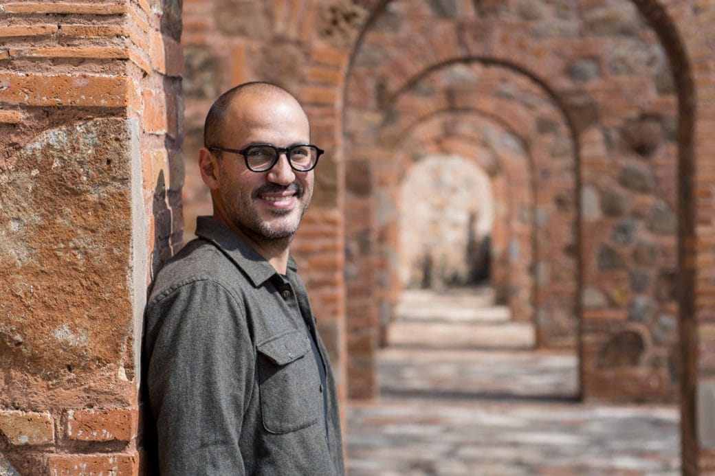 Juan Pablo stands to the left of multiple brick archways.