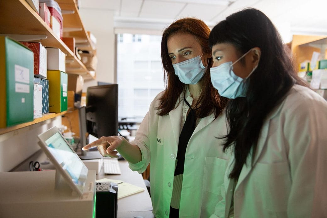 Silvi Rouskin points to a scientific equipment monitor while a lab student looks on.