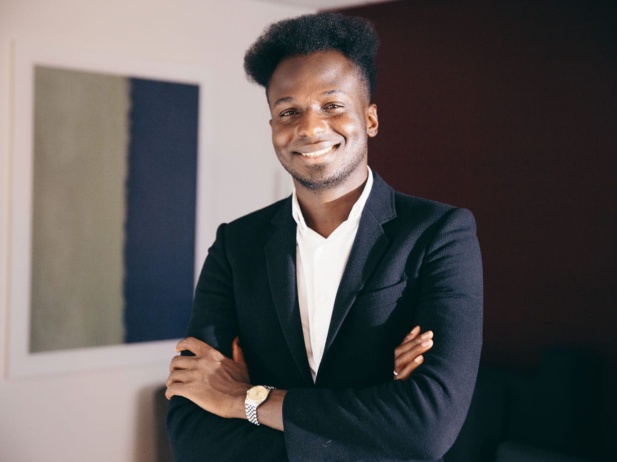 Ibrahim Cissé with a big smile, arms folded, and a black blazer.