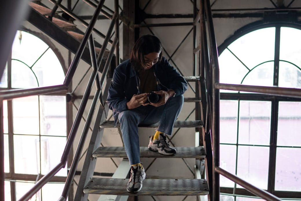Miko Revereza sitting on the metal stairs of a warehouse inspecting his camera.