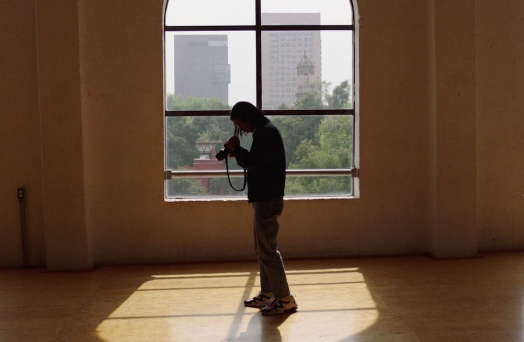 Miko Revereza stands in front of a bright window looking into his camera.