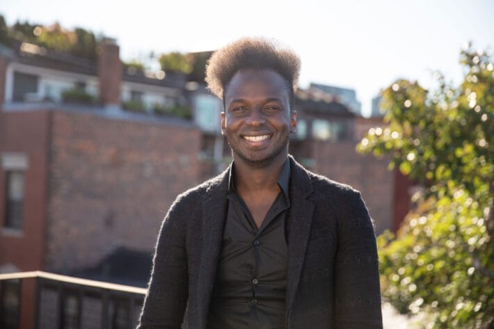 Ibrahim Cissé wearing a black blazer and shirt, smiles standing on a rooftop.