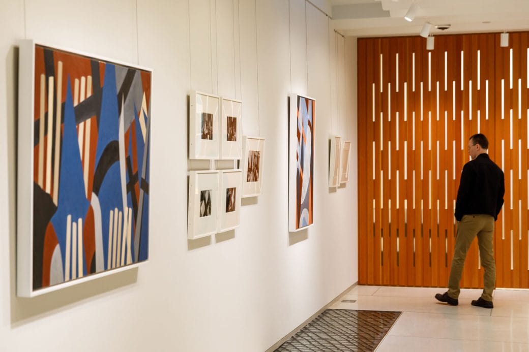 The second floor gallery space with multiple works on the walls, and the decorative wooden exterior of the boardroom. 