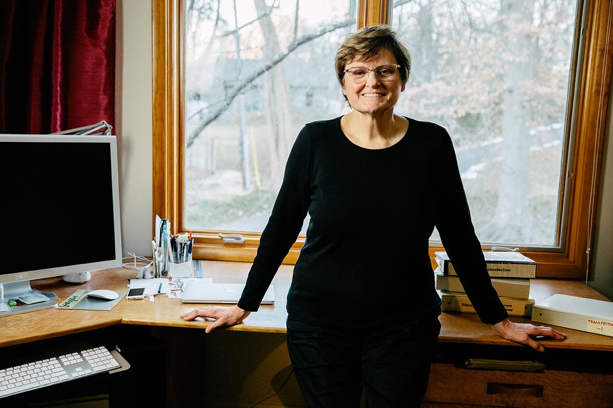 Katalin Karikó standing and leaning against a desk.