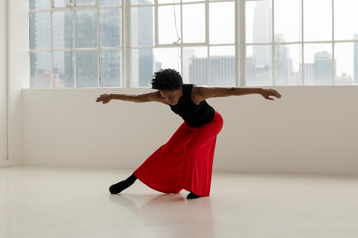 Tamisha Guy dancing in front of a wall of windows in a studio.