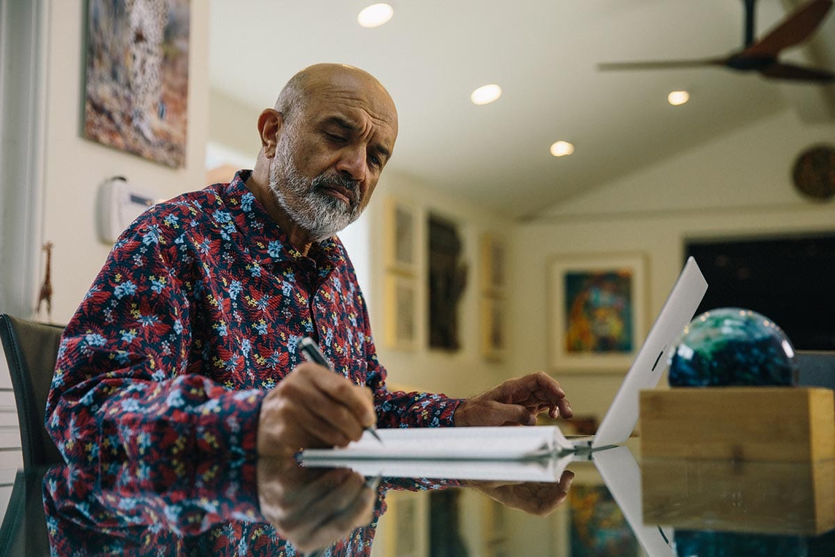 Vishva M. Dixit writing in a notebook at a desk.