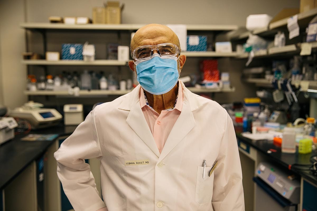 Vishva M. Dixit, in a white lab coat and mask, in his lab at Genentech.