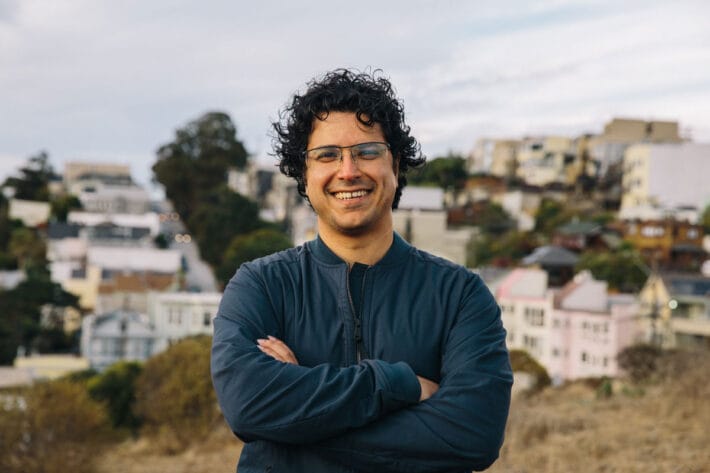 Hani Goodarzi stands in a park with arms folded and smiles.