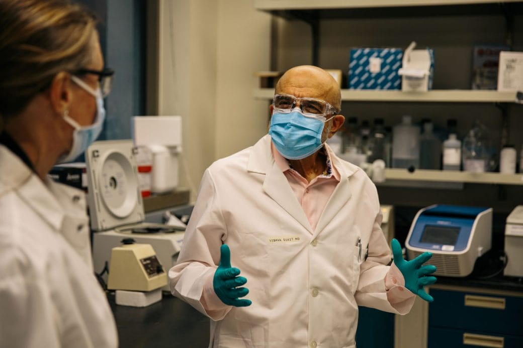 Vishva Dixit in a lab coat, gloves and a mask with a colleague.