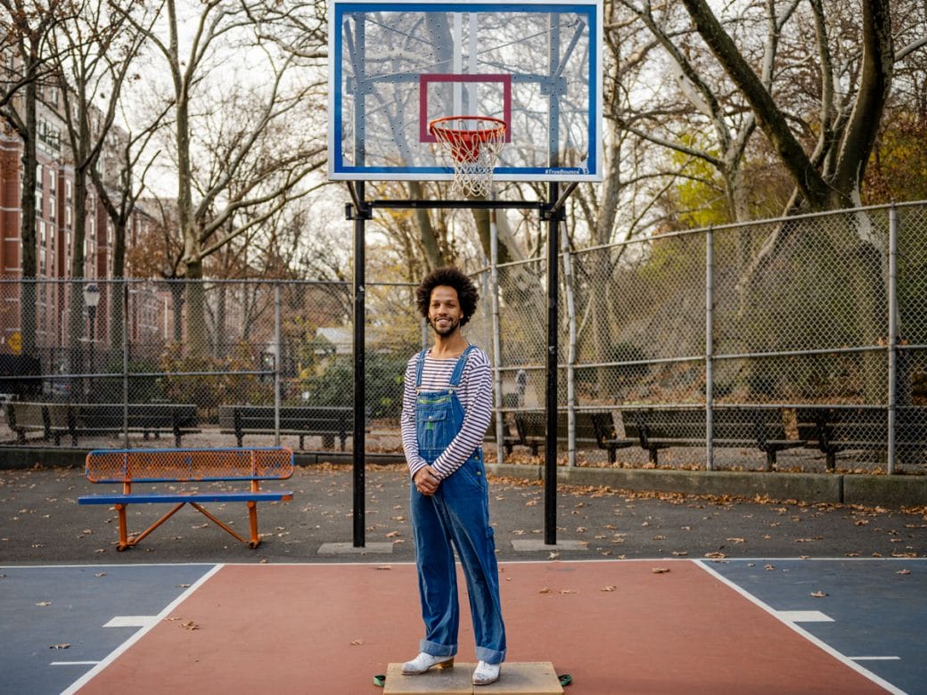 Leonardo Sandoval in overalls smiling on a basketball court.