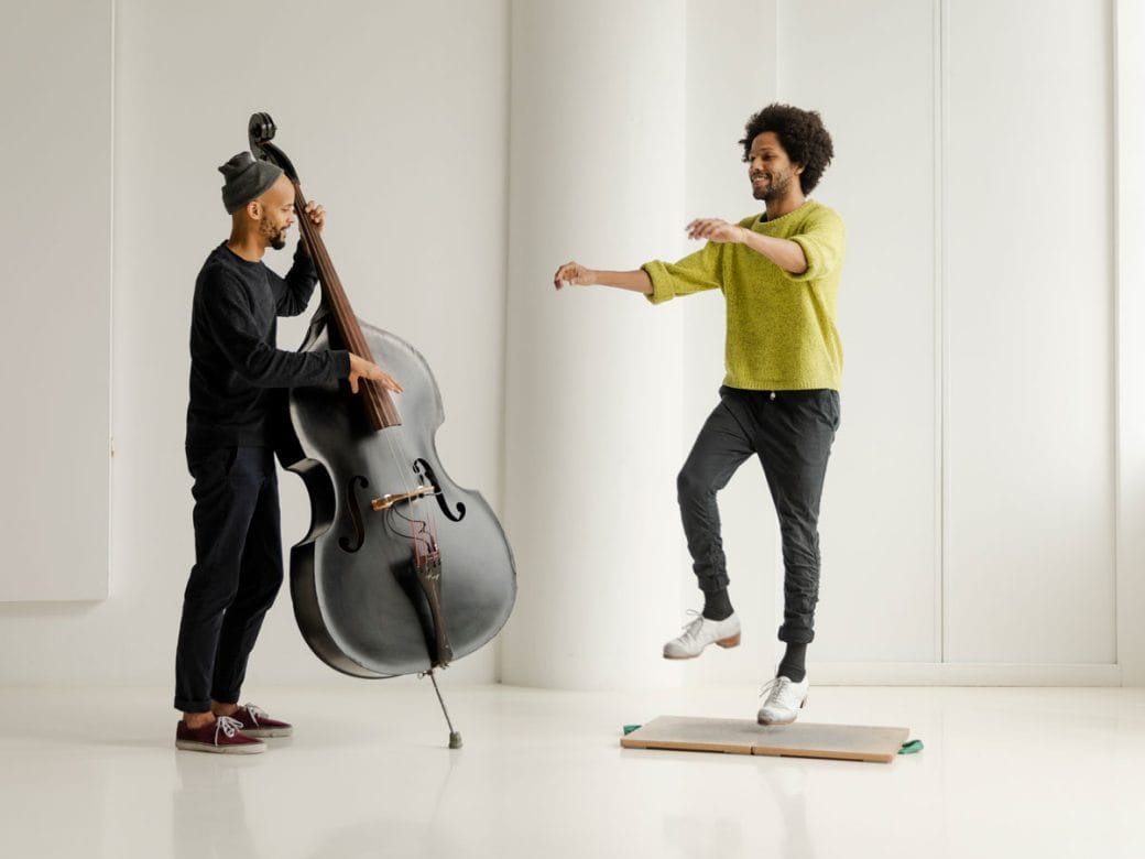 Leonardo Sandoval in a yellow sweater tap dancing next to his colleague playing a standup bass.