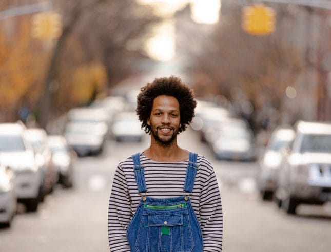Leonardo Sandoval wearing overalls standing in the middle of a street.