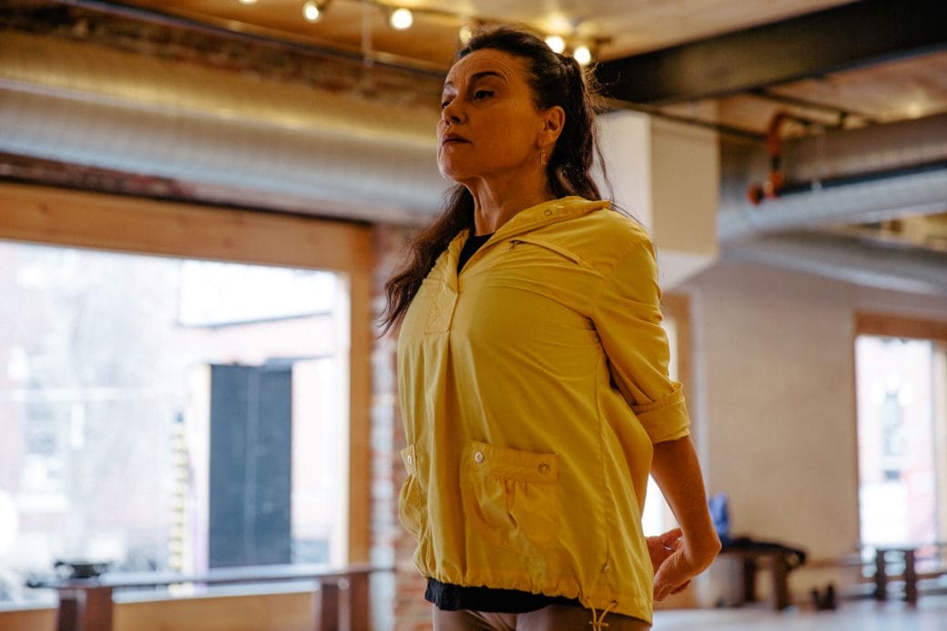 Soledad Barrio in a yellow jacket stretching with her arms behind her back.