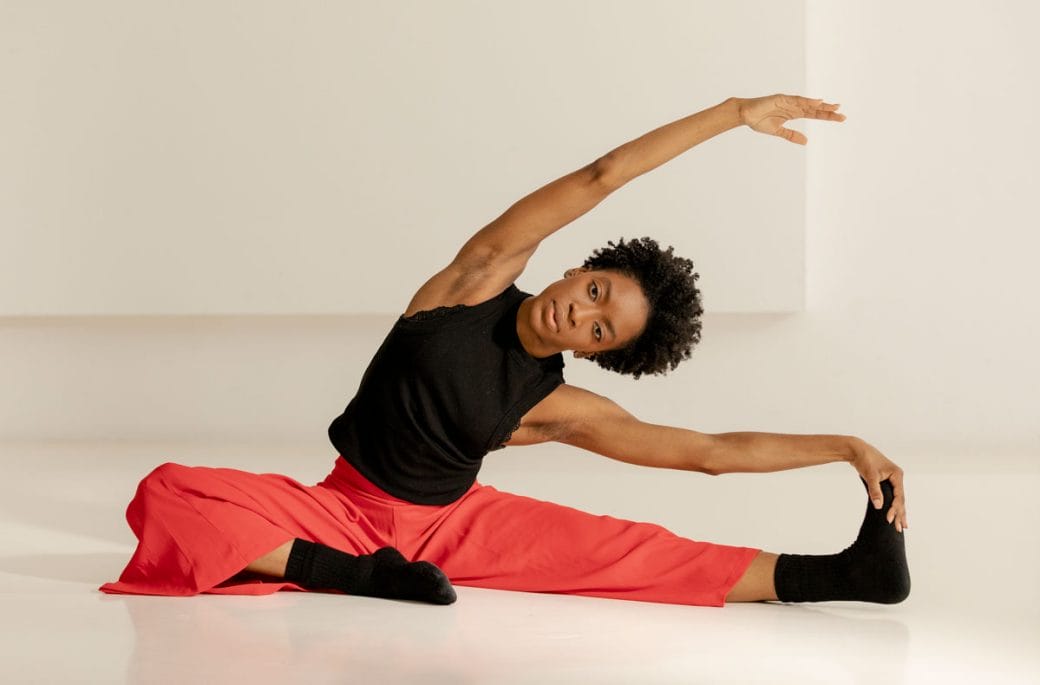 Tamisha Guy in black shirt and red pants stretching.