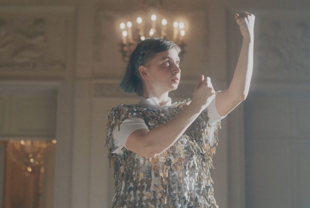 Alice Gosti with her arms raised in fists in front of a chandelier.