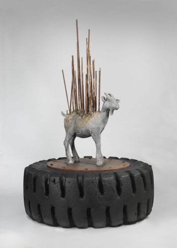 Cast bronze sculpture of a goat with rebar on top of a tire.