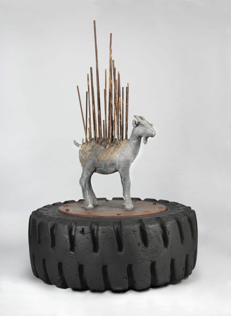 A goat sculpture stands on top of a large tire.